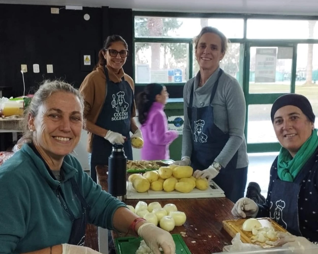 Voluntarias de Cocina Solidaria pelando papas y cebollas con delantales del proyecto