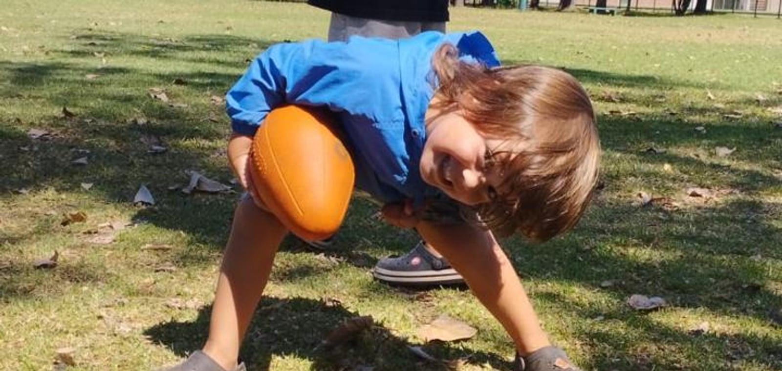 Un nene agachado sosteniendo una pelota de rugby
