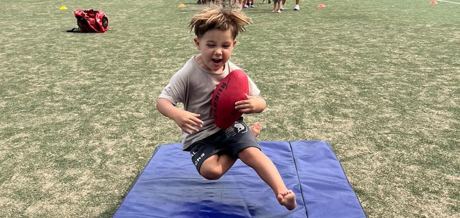 Un nene saltando con una pelota de rugby sobre un colchón