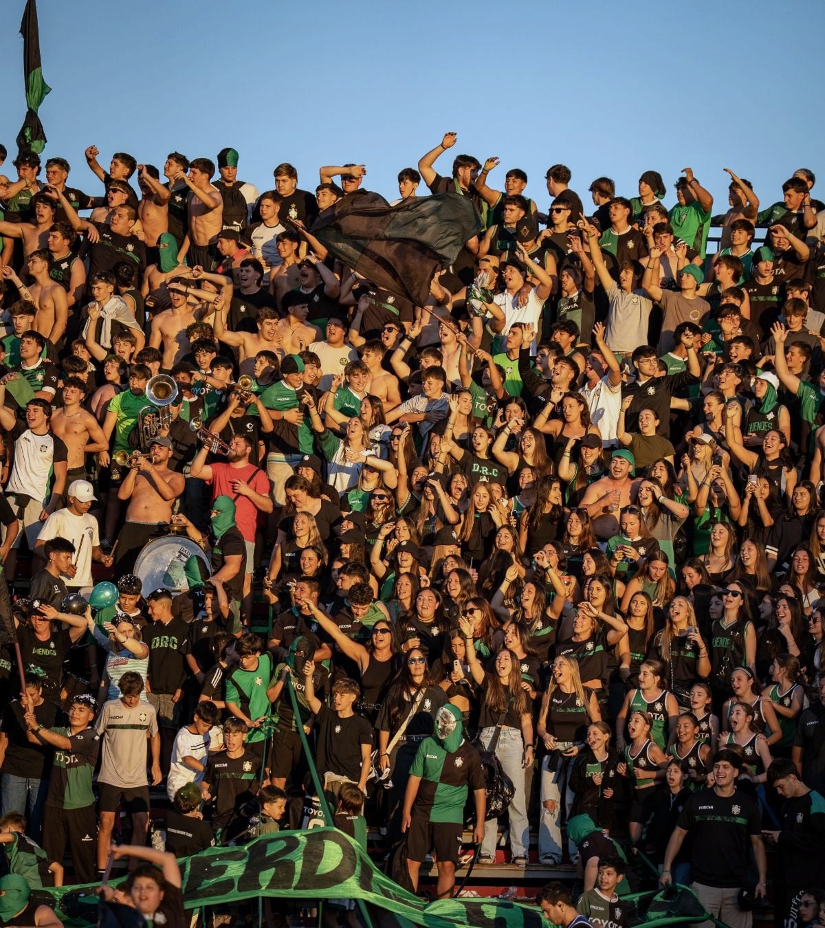 Hinchada de Duendes alentando en la tribuna al atardecer